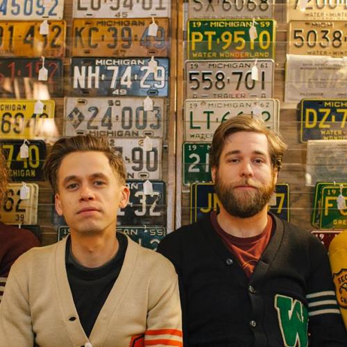 The four members of The Go Rounds sitting in front of a wall of Michigan license plates